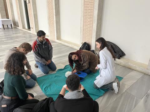 Eğitime katılan bir üniversite öğrencisinin ilk yardım uygulamasını maket üzerinden denemesini gösteren bir görsel .